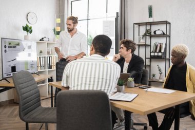 Multiracial male business people having briefing about financial situation at company. Caucasian man pointing on glass board with various graphs and charts. Cooperation and brainstorming concept.