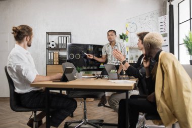 Team of multicultural male traders having negotiation at office room with modern gadgets and papers. Men accounting money and analysing graphs together during working time.