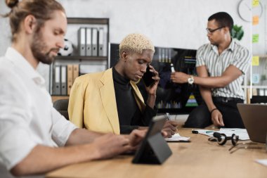 Focused african man speaks on the phone while his male colleagues listening speech of african american businessman. Company managers working at office room. Deadlines concept.