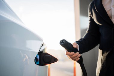 Erkek eliyle elektrik kablosunu açık hava elektrik santralinde beyaz elektrikli arabaya yerleştiriyor. Arka plan bulanık. Bilinçli sahibi olan çevre dostu ulaşım.