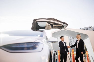 Asyalı tezgahtar kadın müşteriyle başarılı bir anlaşma için tokalaşıyor. Kendine güvenen beyaz, şık iş kadını yeni elektrikli araba alıyor..