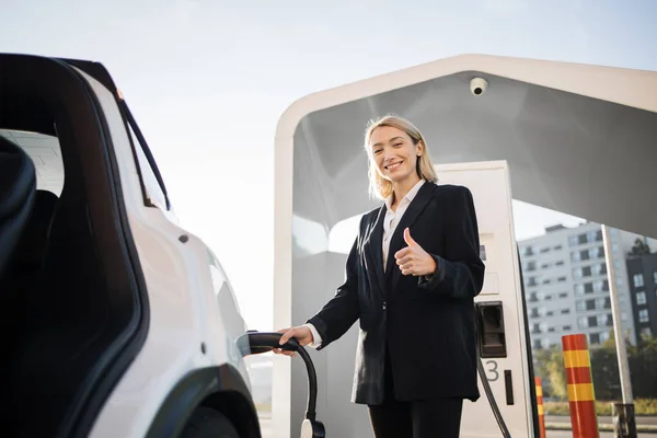 Geschäftsfrau Lädt Batterie Eines Weißen Elektroautos Auf Und Telefoniert Freien — Stockfoto