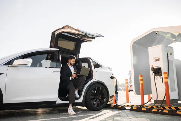 Ein Stilvoller Unternehmer Mit Drahtlosem Laptop Beim Laden Von Elektroautos — Stockfoto