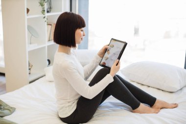 Gündelik giyinmiş çekici genç bir kadın dijital tablet kullanarak öğle yemeğinde indirimli yemek alıyor. Koyu renk saçlı kadın, büyük şehir yaşam tarzı için modern aletlerin tadını çıkarıyor..