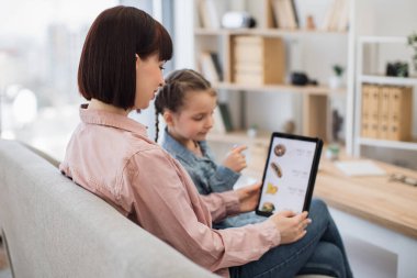Gülümseyen müşterilerin indirimli olarak fast food yemeyi seçtiği internet sitesini kapatın ve evde dinlenin. Huzurlu kadın ve kız tabletle önceden pişirilmiş yemekler alırken birlikte kaliteli zaman geçiriyorlar..