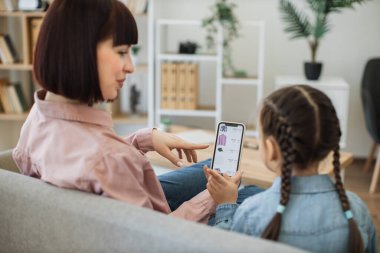 Moda butiğinin e-ticaret sitesinde sörf yapan ve indirim arayan genç bayanların arka planı. Anne ve kızı akıllı telefon kullanarak internet üzerinden kıyafet alırken evde vakit geçiriyorlar..