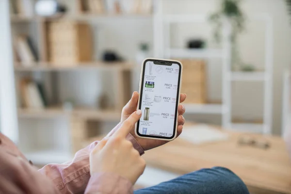 stock image Close up of lady using smartphone for browsing online beauty store while staying at home. Young woman focusing on mobile screen where new branded cosmetics being available at generous discount.