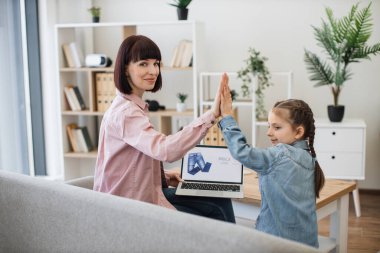 Küçük mutlu anne ve kız birbirlerine beşlik çakarken taşınabilir laptoptan giysi sipariş ediyorlar. Satış sezonunda alışveriş zamanı. Modern teknolojiye uygunluk.