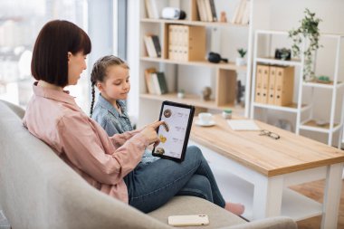 Rahatlamış anne ve kız, kapalı alanda eğlenirken restoran yemekleri ve tablet uygulamalarıyla ilgili e-ticaret teklifleri arıyor. Verimli çevrimiçi müşteriler ürünlerdeki indirimli fiyatlara el koyuyor.