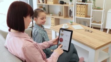 Rahatlamış anne ve kız, kapalı alanda eğlenirken restoran yemekleri ve tablet uygulamalarıyla ilgili e-ticaret teklifleri arıyor. Verimli çevrimiçi müşteriler ürünlerdeki indirimli fiyatlara el koyuyor.