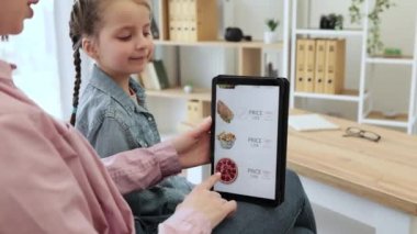 Gülümseyen müşterilerin indirimli olarak fast food yemeyi seçtiği internet sitesini kapatın ve evde dinlenin. Huzurlu kadın ve kız tabletle önceden pişirilmiş yemekler alırken birlikte kaliteli zaman geçiriyorlar..