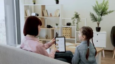 Genç beyaz kadın ve kız güzel bir dairede oturuyor ve tablet ekranda internetten fast food dağıtım uygulamalarına işaret veriyorlar. Gülümseyen kadınlar omuzlarının üzerinden bakıyor ve e-kuyruğunu onaylıyorlar..