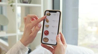 Kafkasyalı kadının ellerini kapat. Modern akıllı telefonu kullanarak evde otururken internetten indirimli fast food siparişi veriyor. İnsanlar, aletler ve tüketim anlayışı.