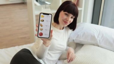 Rahat giyinen hoş beyaz kadın evde otururken internetten fast food ve indirimli yemek sipariş etmek için modern akıllı telefon kullanıyor. İnsanlar, aletler ve tüketim anlayışı.