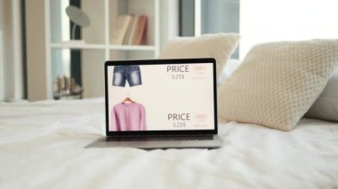 Ekranda online giyim mağazası olan modern kablosuz dizüstü bilgisayar beyaz çarşaflı rahat bir yatağa yerleştiriliyor. Online sipariş için yüzde 15 ve yüzde 25 indirim. Tüketim kavramı.