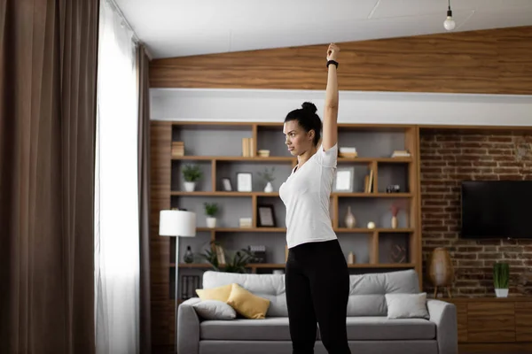 stock image Focused african woman in sport clothes doing fitness exercises with hands during workout at home. Active young brunette enjoying morning training for staying fit and healthy.