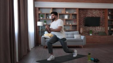 Spor kıyafetli Hintli erkek sporcu evde düzenli antrenman yaparken yoga minderinde mekik çekiyor. Arka planda modern oturma odası. Sağlıklı yaşam tarzı kavramı.