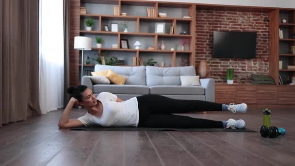 多种族迷人的女人穿着运动服躺在瑜伽垫上 躺在客厅里抬腿 身体护理 健康生活方式和定期锻炼的概念 — 图库视频影像