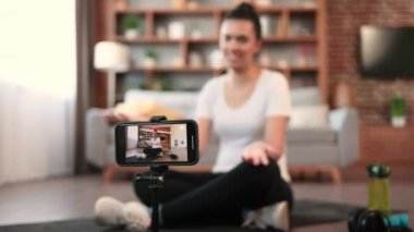 Tripod üzerine modern cihazın seçici odak noktası spor giyimli aktif Afro-Amerikan kadını kameraya konuşurken içeride dinleniyor. Kişisel koç rehberlik eğitimi çevrimiçi.