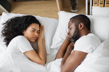 Modern apartmandaki yumuşak beyaz yatakta uyuyan Afro-Amerikan çiftlerin en sevilen görüntüsü. Rahat, güzel bir kadın ve yakışıklı sakallı bir adam. Parlak yatak odasında dinleniyorlar..