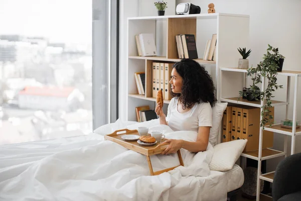 아름다운 아가씨가 맛있는 크로와 아침에 침실의 파노라마 창문턱에서 즐거운 시간을 — 스톡 사진