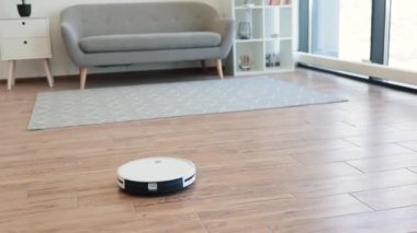 Gelişmiş robotik elektrik süpürgesi güneşli bir günde sıcak bir dairede havadar oturma odasını süpürüyor. Verimli ev aletleri sert zemini ve yumuşak halıyı uzaktan kumandayla ya da telefon uygulaması ile düzenli tutar.