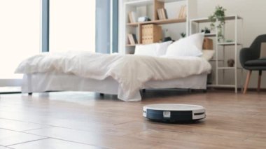 Akıllı robot süpürge, ev sahipleri yokken geniş yatak odasındaki lamine zeminde otomatik temizlik yapıyor. Ev işlerini devralmak ve insanların diğer görevlere odaklanmasına yardımcı olmak için teknolojik gereçler..