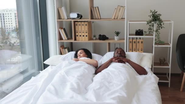 深爱着身穿休闲装的非洲裔美国夫妇 他们在睡后伸展四肢 同时还躺在明亮的卧房床上 在现代公寓里 松懈的男男女女开始了新的阳光灿烂的一天 — 图库视频影像