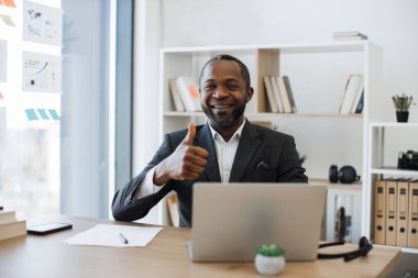 Akıllı takım elbiseli, modern aletlerle masa başında oturan kendine güvenen ofis yöneticisi. Ofisteki laptop ekranından bilgi yazan odaklanmış çok kültürlü bir işçi..
