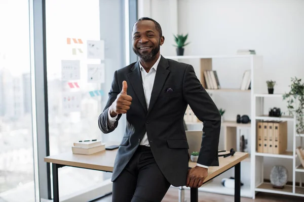 Close up of successful businessman in formal attire smiling at camera while working in modern work environment. Cheerful african american executive manager enjoying his work-life balance at office.