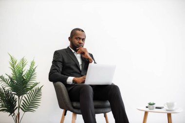 Resmi olarak çalışkan bir Afro-Amerikan çalışanı ofisteki kablosuz dizüstü bilgisayarda modern minimalist tasarımı yazarken kameraya samimi bir şekilde gülümser. İnsanlar, iş ve teknoloji kavramı.