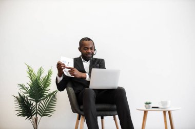 Uzman bir Afrikalı Amerikalı finansör modern laptopta online video toplantısı sırasında grafikler ve grafikler sunuyor. Resmi olarak giyinmiş, kulaklıklı bir adam ofiste oturuyor ve uzaktan görüşme yapıyor..