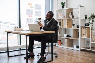 Modern ofisteki ortaklarla çevrimiçi görüşmeler yapan başarılı bir iş adamı. Afrika kökenli Amerikalı adam mali raporlar sırasında grafikler ve grafikler gösteriyor.