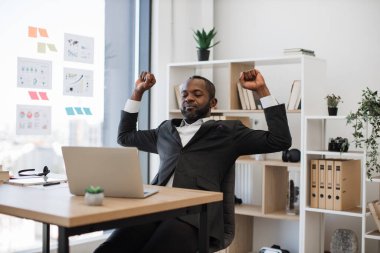 Uykulu ve yorgun Afrikalı Amerikalı resmi görevli ofis bilgisayarında saatlerce çalıştıktan sonra esniyor ve kollarını esnetiyor. İnsan kavramı, teknoloji ve aşırı çalışma.