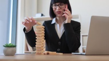 Ofis arka planında akıllı telefondan konuşurken elinde Jenga oyununun tahta bloğu olan gözlüklü beyaz bir iş kadını. İşteki kule inşaatı ile yaratıcı yönetici eğitim kontrol riski.