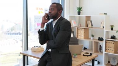 Havai iş yerindeki ofis masasına yaslanırken resmi giyinmiş kendine güvenen Afro-Amerikan işadamı cep telefonuyla konuşuyor. Proje yöneticisi ofisteki meslektaşlarıyla yeni programı tartışıyor.