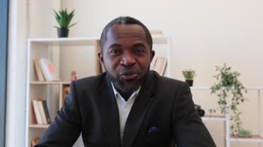 Siyahi takım elbiseli arkadaş canlısı Afrikalı girişimci video sohbet için kablosuz bilgisayar kullanıyor. İş ortaklarıyla çevrimiçi görüşmede el sallayan yakışıklı genç adam..