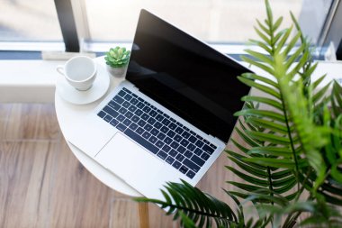 Kablosuz laptop, parlak ofisteki beyaz seramik bardağın yanındaki sehpanın üzerine yerleştirilmiş. Çalışanların rahat ve modern işyeri. İş için teknoloji kavramı.