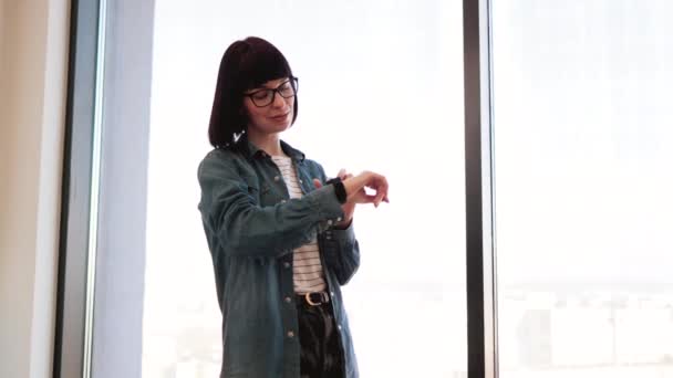 Poważna Biała Kobieta Okularach Dotykająca Ekranu Smartfona Nadgarstku Stojąca Nowoczesnym — Wideo stockowe