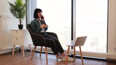 Ofiste kahve molası sırasında akıllı telefonla konuşan günlük kıyafetli mutlu beyaz kadın. Telefon görüşmesi sırasında sosyal ağlar kullanan gözlüklü bir iş kadını..