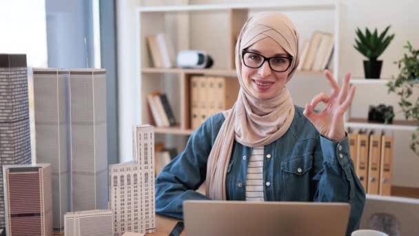 年轻的穆斯林妇女戴着头巾和眼镜坐在房地产商的写字台前 在安排购买住宅物业时 使用无线技术的有效地产代理 — 图库视频影像