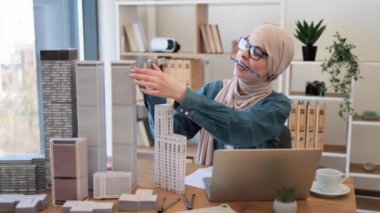 Geleneksel tesettürlü profesyonel Müslüman iş kadını ofiste çalışırken cetvel kullanarak model oluşturma ölçümleri yapıyor. Yaratıcı tasarımcı dizüstü bilgisayarla ayrıntıların doğruluğunu kontrol ediyor.
