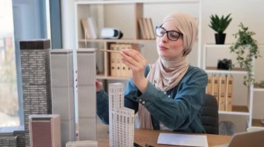 Başörtüsü içinde büyüleyici bir Arap kadın ve sıradan giysiler içinde pusula tutarken ofis içinde dizüstü bilgisayarla yazı masasında oturuyor. Mimari planlarda profesyonel ölçümler tasarla.