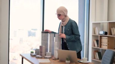 Üzerinde dizüstü bilgisayarla ofis masasının arkasında dururken tesettürlü müslüman iş kadını binalara dokunuyor. Geniş iş işyerindeki gökdelenin deneyimli tasarımcı bitirme modeli.