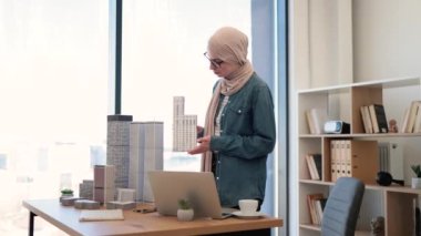 Geleneksel tesettürlü çekici bir Arap kadın modern dizüstü bilgisayarda çalışırken yazı masasında maket tutuyor. Mimari proje yöneticisi modern inşaatın planını tasarlıyor.