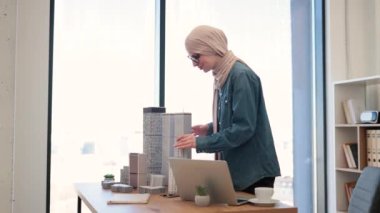 Geleneksel tesettürlü çekici Arap kadın ofiste yazı masasında modelimize dokunurken aynı zamanda modern dizüstü bilgisayarda çalışıyor. Mimari proje yöneticisi modern inşaatın planını tasarlıyor.
