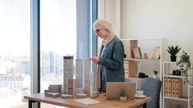 Geleneksel tesettürlü profesyonel Müslüman iş kadını ofiste çalışırken cetvel kullanarak model oluşturma ölçümleri yapıyor. Yaratıcı tasarımcı dizüstü bilgisayarla ayrıntıların doğruluğunu kontrol ediyor.