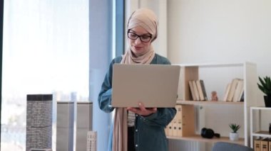 Geleneksel tesettürlü profesyonel Müslüman iş kadını ofiste çalışırken cetvel kullanarak model oluşturma ölçümleri yapıyor. Yaratıcı tasarımcı dizüstü bilgisayarla ayrıntıların doğruluğunu kontrol ediyor.