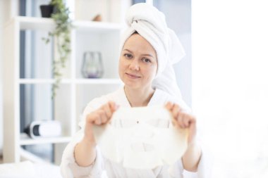 Hafta sonu evde kaplıcanın tadını çıkarırken peçete maskesi takan duştan sonra rahatlamış neşeli kadın. Mutlu beyaz kadın yüz derisinin kullanışlı güzelliğinden faydalanıyor..