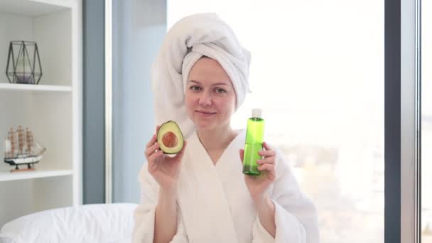 Usmívající Žena Šatech Sprše Prezentující Zelený Avokádo Ovoci Kosmetickém Oleji — Stock video